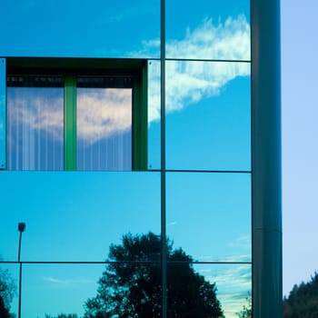 Mirrored image of environment of office building on highly reflective exterior wall with window.