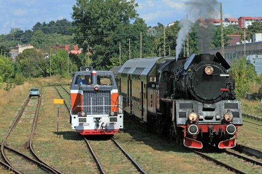 Car, diesel locomotive and old retro steam train standing at the small station

