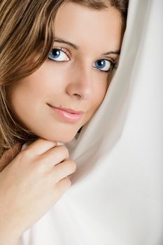 Beautiful young woman peeking behind a white sheet