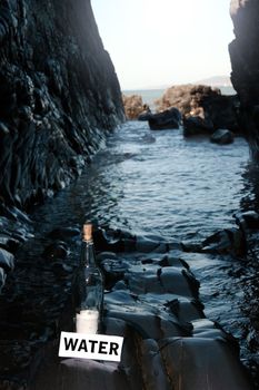 a bottle with a message on water standing on a rocky coastline
