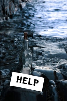 a bottle with a help message label standing on a rocky coastline
