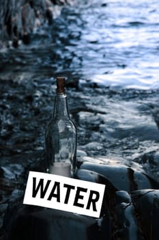a bottle with a message on water standing on a rocky coastline