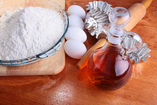 The forms prepared for a batch, and also components: a flour, eggs, oil, on a chopping board with Rolling pin.