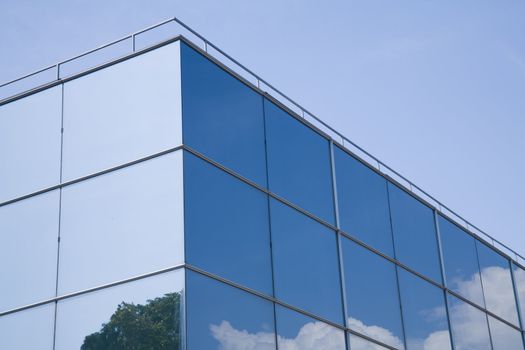 Modern glass building with trees and clouds reflected on it.