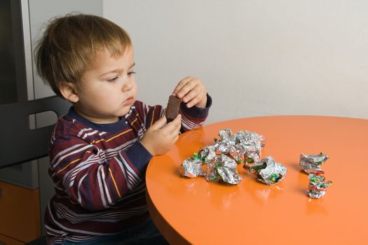 Little boy sitting at a table eating chocolates