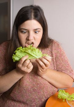 Stout woman trying to eat a leaf of lettuce