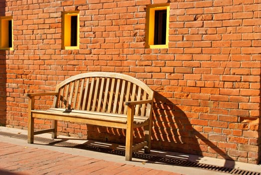 An old wooden bench sits by a worn orange brick wall with three yellow windows