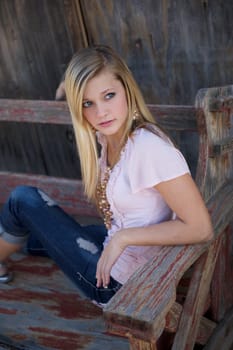 A beautiful blonde gilr sitting on an old wooden bench with torn jeans and a pink blouse