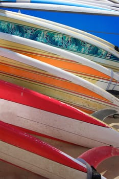 A row of brightly colored renal surfboards laying on the sand in Hawaii