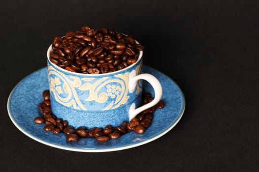 A cup and saucer overflowing with dark roasted coffee beans