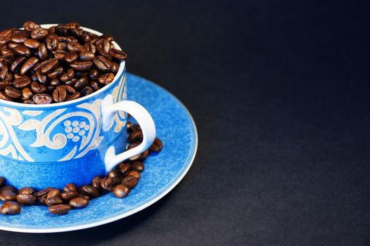 Dark roasted coffee beans in a blue cup and saucer