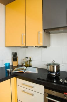 Cooking in colorful modern kitchen with cookbook and pan on gas-burner