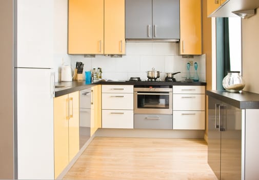 View into colorful modern kitchen in black, yellow and grey with wooden floor - horizontal