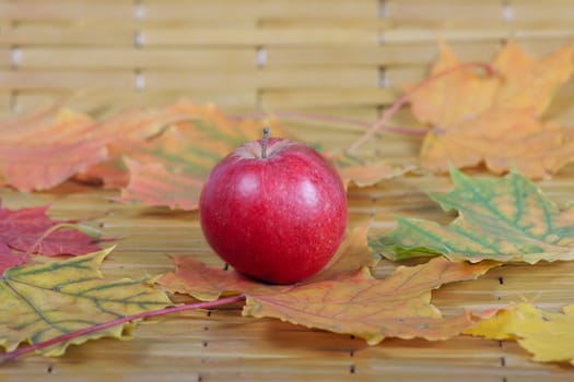 The red apple which has been removed on a bamboo napkin in an environment of autumn leaves