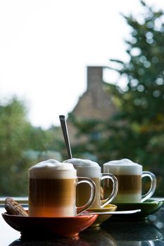 Black granite kitchen dresser with three glass mugs "cafe au lait", colorful saucers and view through window - vertical image