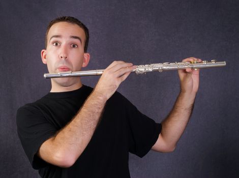 A young man playing a metal flute which is a wind instrument