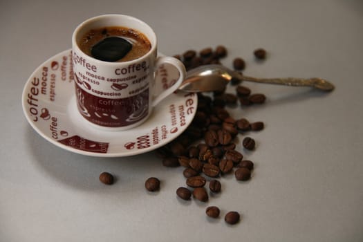 Cup of coffee with saucer, spoon and some coffe beans