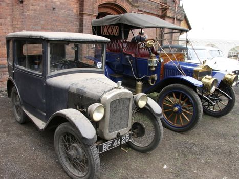 two old vintage cars  the small one is wooden framed and covered in leather
