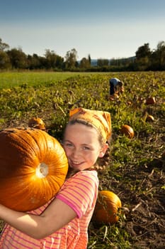 young girl in field holding large pumpkind