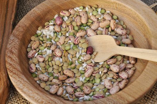 Wooden bowl within beans, lentils, chick-peas and rice and a wooden ladle