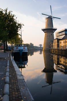 Mill and ship with reflection in water at sunrise - vertical image