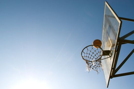 Basketball just before dropping into the net in a basketball game on an open court at sunset