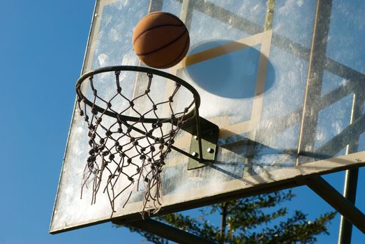 Basketball dropping into the net in a basketball game on an open court at sunset