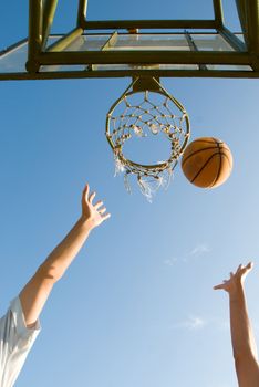 Boys challenging for the ball under the net in a casual game of basketball on an open court at sunset