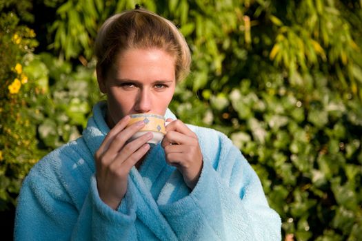 Beautiful blond woman sitting in the early morning sunshine enjoying her coffee