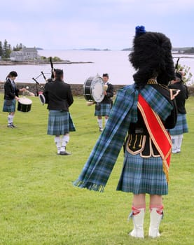 Drum Major of the Maine St. Andrews Pipes and Drums, wearing colorful kilt and sash, directing drummers and bagpipers at seaside