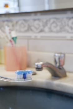 Detail shot of a tooth brush with tooth paste on it and basin in the blurred background
