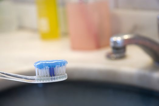 Detail shot of a tooth brush with tooth paste on it and basin in the blurred background