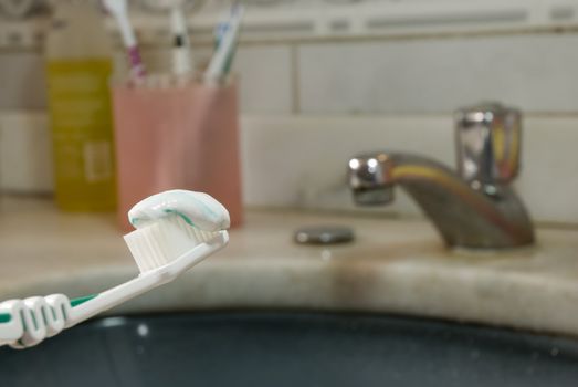 Detail shot of a tooth brush with tooth paste on it and basin in the blurred background