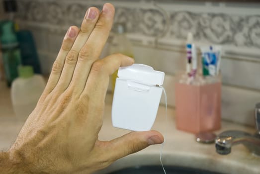 Detail shot of a male hand holding a blank dental floss box, with basin in the blurred background.