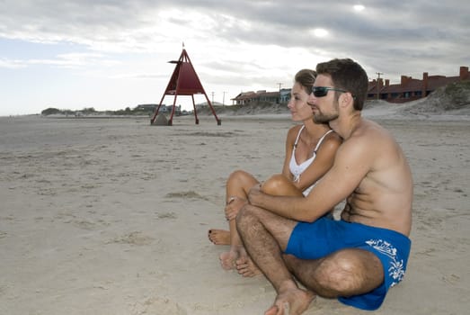 Young healthy couple sitted in the sand, looking out into the sea (side shot).