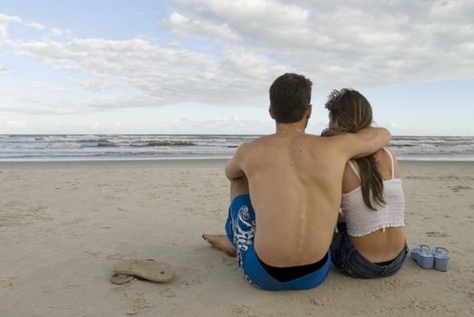Young healthy couple sitted in the sand, looking out into the sea.
