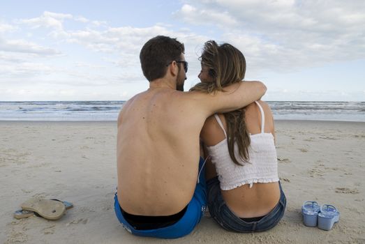 Young healthy couple sitted in the sand, looking out into the sea.