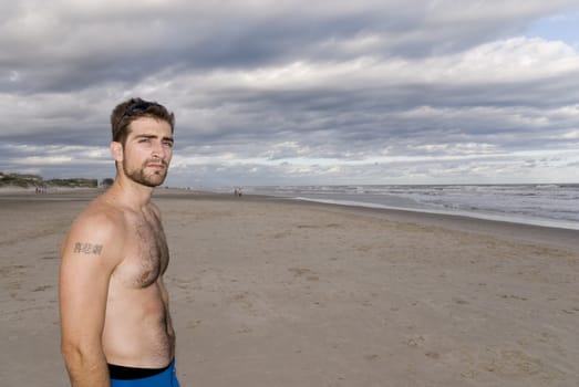 Handsome young man in the sand (late afternoon), with cloudy sky.