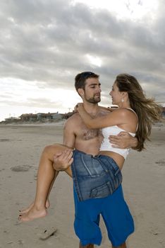 Young, fit, happy couple in the beach. Man holding girl.