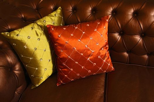 Two small embroidered pillows on a brown leather sofa