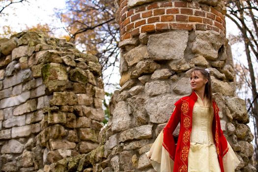 lady in medieval red dress standing near old wall
