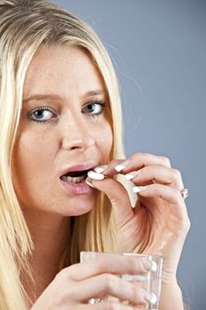 blonde woman taking a pill with a glass of water