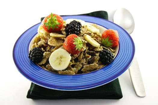 Crunchy looking delicious bran flakes and juicy fruit in a blue bowl with a spoon on a black napkin on a white background
