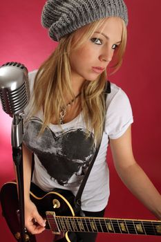 Photo of a gorgeous blond playing an electric guitar and about to sing into a retro microphone.