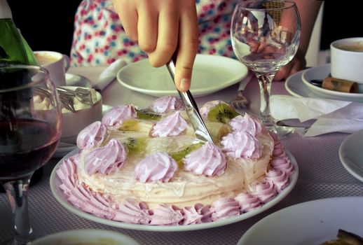 Cutting the cake, topping is a flowers of cream and freshes fruits.