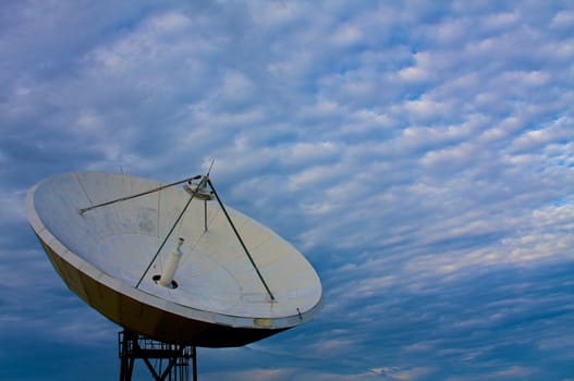 A large satellite dish points into a cloudy blue sky
