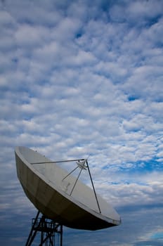 A large satellite dish points into a cloudy blue sky