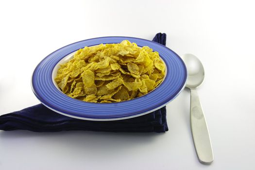 Golden crisp cornflakes in a round blue bowl with a black napkin and a spoon on a white background