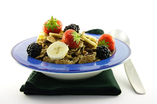 Crunchy looking delicious bran flakes and juicy fruit in a blue bowl with a spoon on a black napkin on a white background