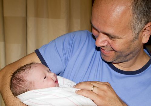 Dad meets her daughter firs time, both happy as can be, looking at each other.